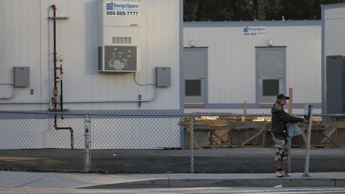 A man crosses the street near Arcadia and Alameda streets. Behind him are the first emergency homeless shelters at El Pueblo.