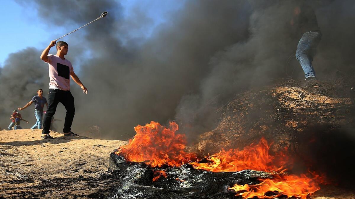 A Palestinian protester uses a slingshot next to burning tires during a demonstration at the Israel-Gaza border, east of Khan Yunis in the southern Gaza Strip on Aug. 10.