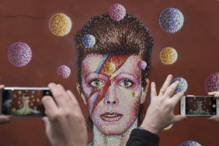 People take photographs of a mural of David Bowie in the London district of Brixton, where the British singer was born. Bowie died Sunday at age 69.