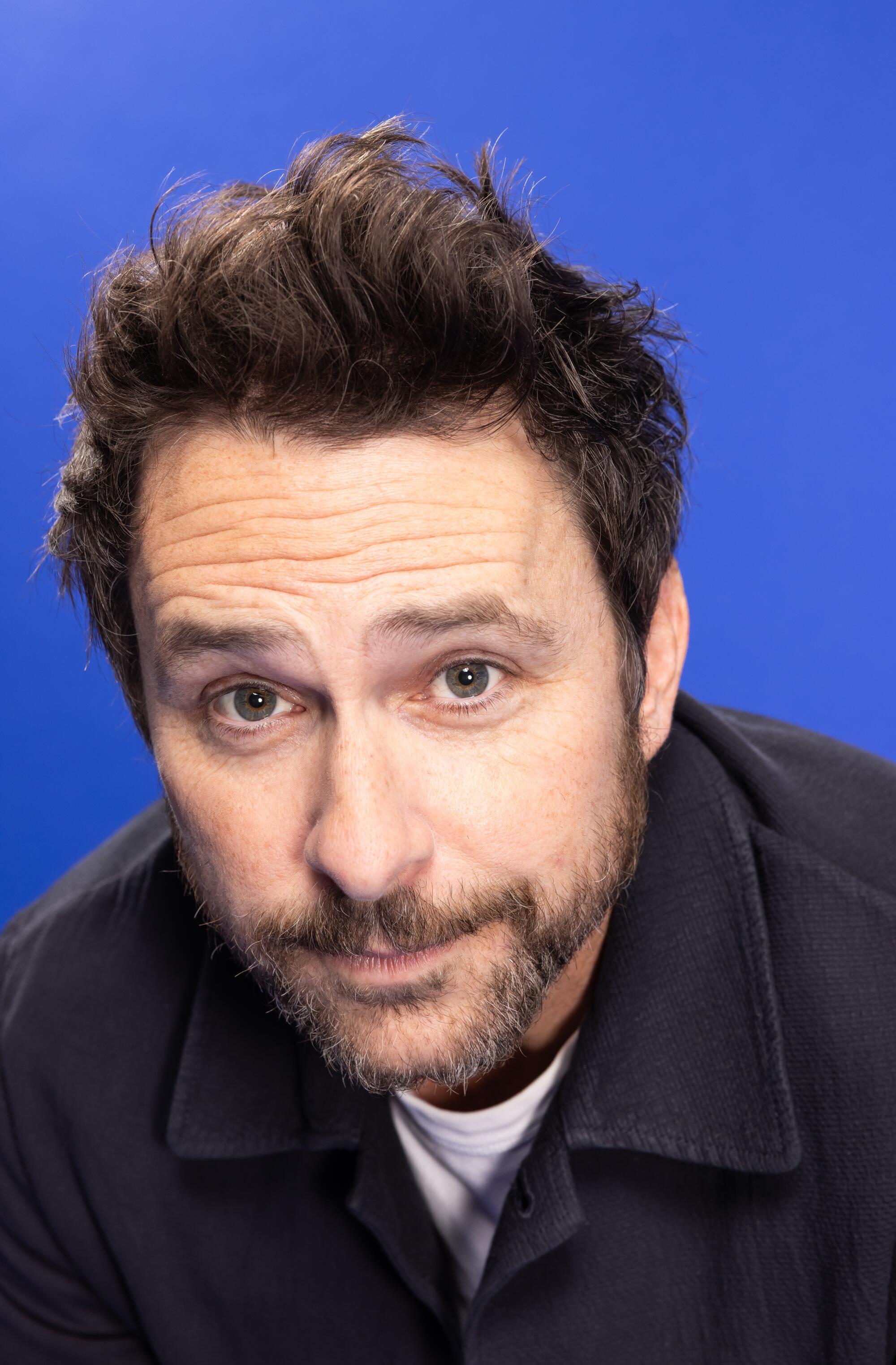 A headshot of a man with short dark hair and a beard in a black jacket.