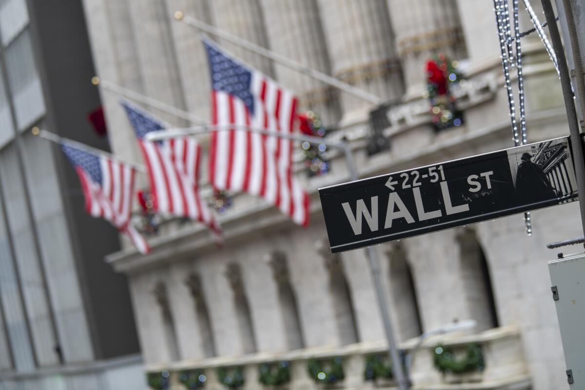 Three American flags are to the left of a Wall Street street sign outside the New York Stock Exchange.