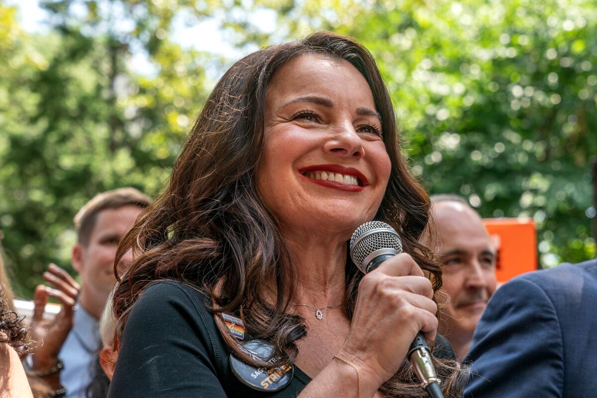 Fran Drescher smiles at an outdoor rally as she holds up a microphone.