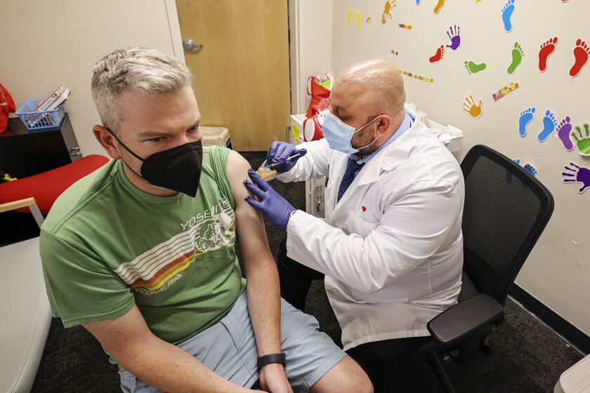 El Cajon, CA - September 16: Pharmacist Saif Namiq (right) administers a COVID booster shot to Colm Driscoll at a CVS drug store on Friday, Sept. 16, 2022 in El Cajon, CA. Driscoll also got a flu shot during the visit. (Eduardo Contreras / The San Diego Union-Tribune)