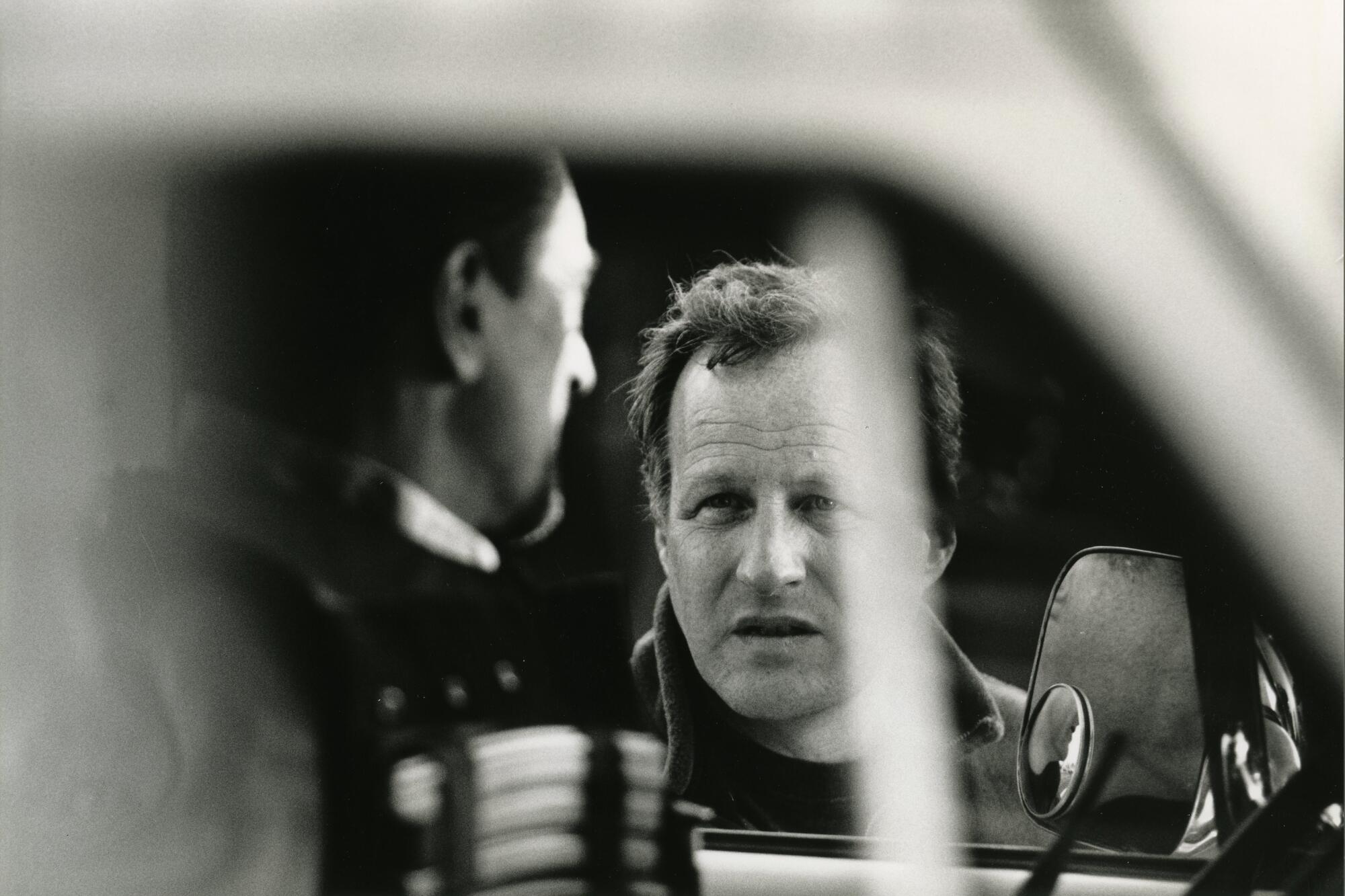 Black and white photo of a man at a drivers seat and a man looking into his window 