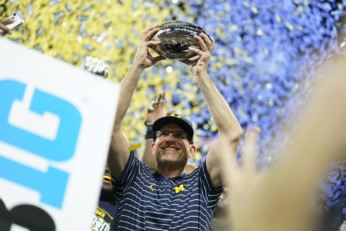 Michigan coach Jim Harbaugh hoists a trophy.