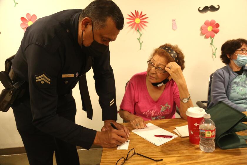 LOS ANGELES, CA - JUNE 15, 2023 - LAPD Detective Albert Smith leaves his card with Marta Barillas, who was robbed recently, after a presentation about financial scams and physical abuse against seniors at St. Barnabas Senior Services in Los Angeles on June 15, 2023. Members of the LAPD and a manager with Adult Protective Services gave a presentation to help educate seniors of possible scams and what resources are available to them. (Genaro Molina / Los Angeles Times)
