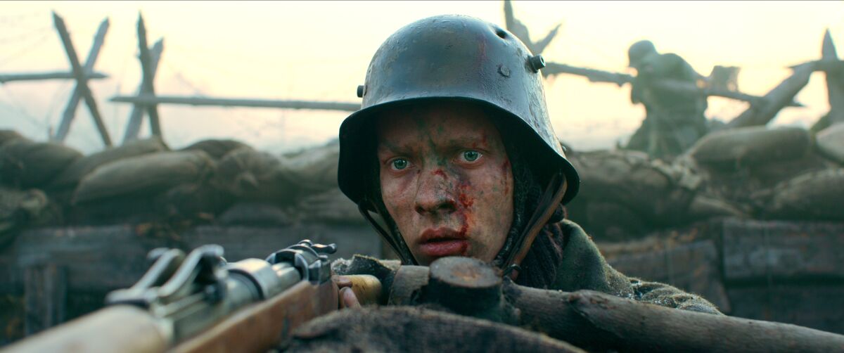 Close-up of a soldier in a trench, with blood and dirt on his face, holding a gun.