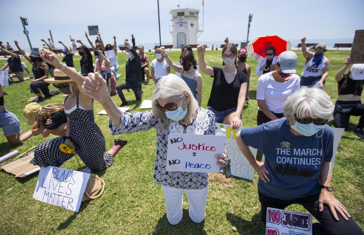 Margo Ganson, left, and Molly Pritchard kneel for nine minutes during a protest at Main Beach in Laguna Beach on Wednesday.