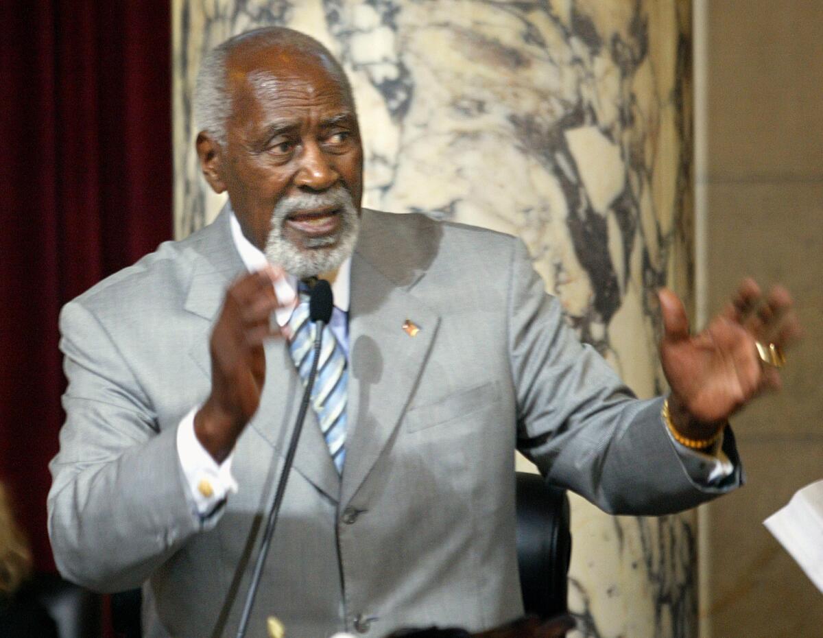 A man in a gray suit speaks into a microphone.