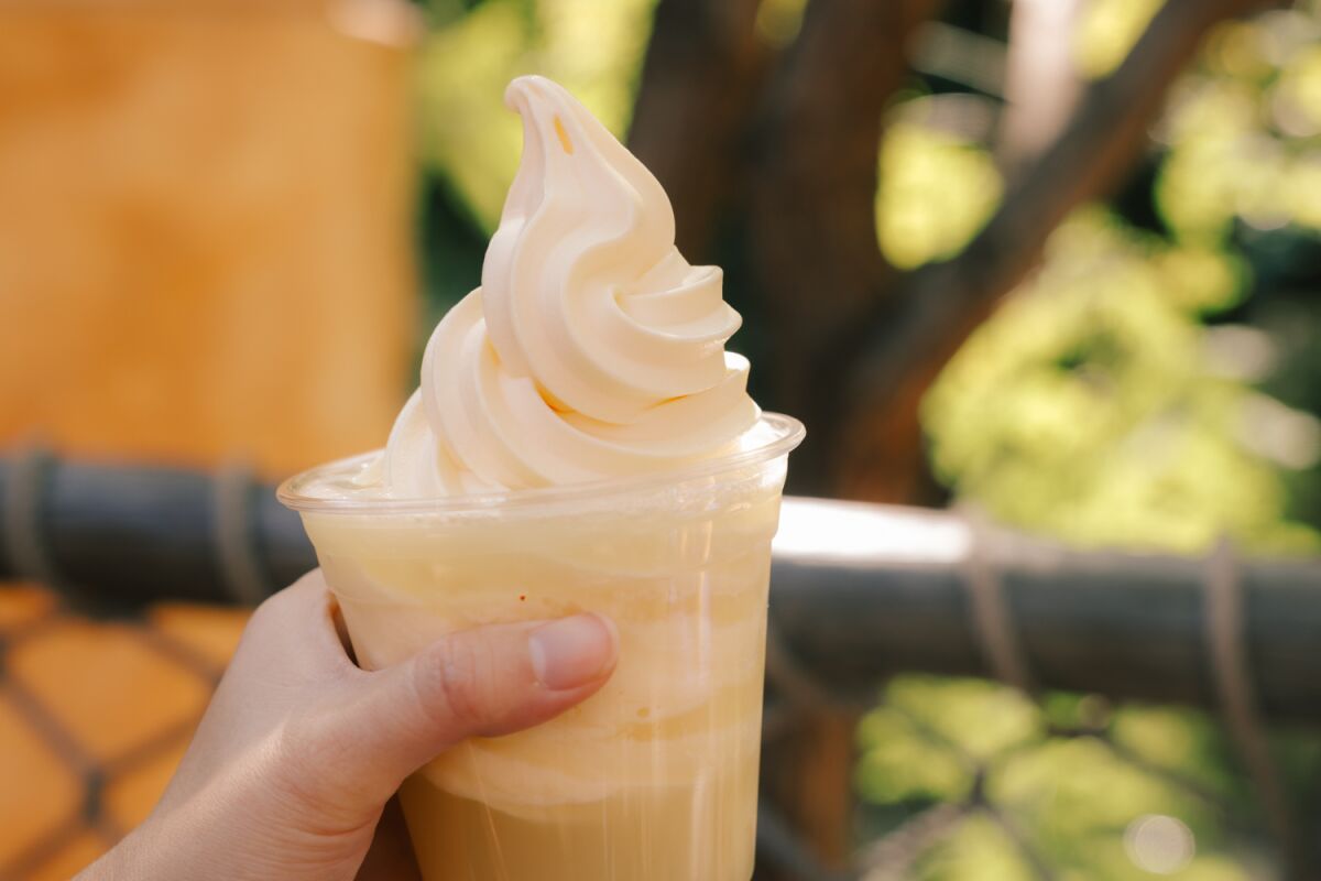 A hand holds a Dole Whip Float made with pineapple juice and topped with Dole Whip pineapple soft serve 