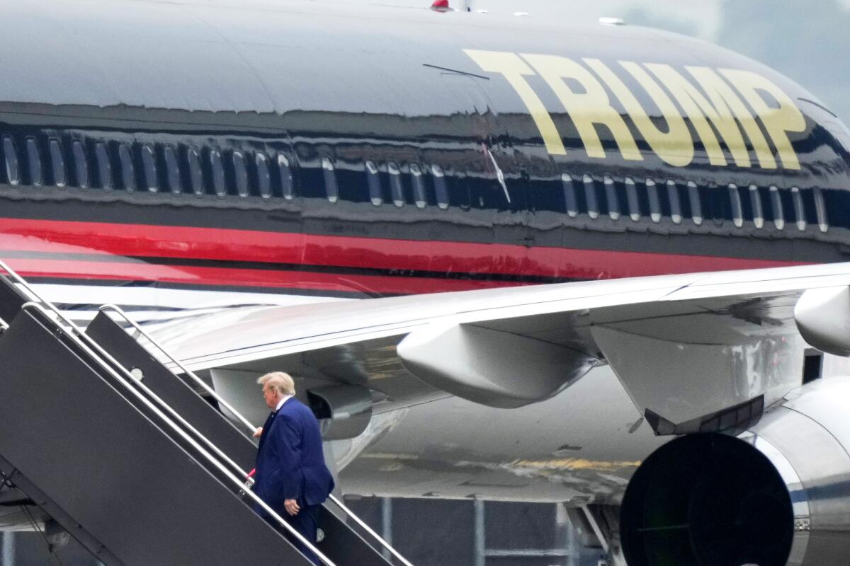 Walking up the stairs, a small figure of Donald Trump boards a airplane with "trump" written in gold letters.