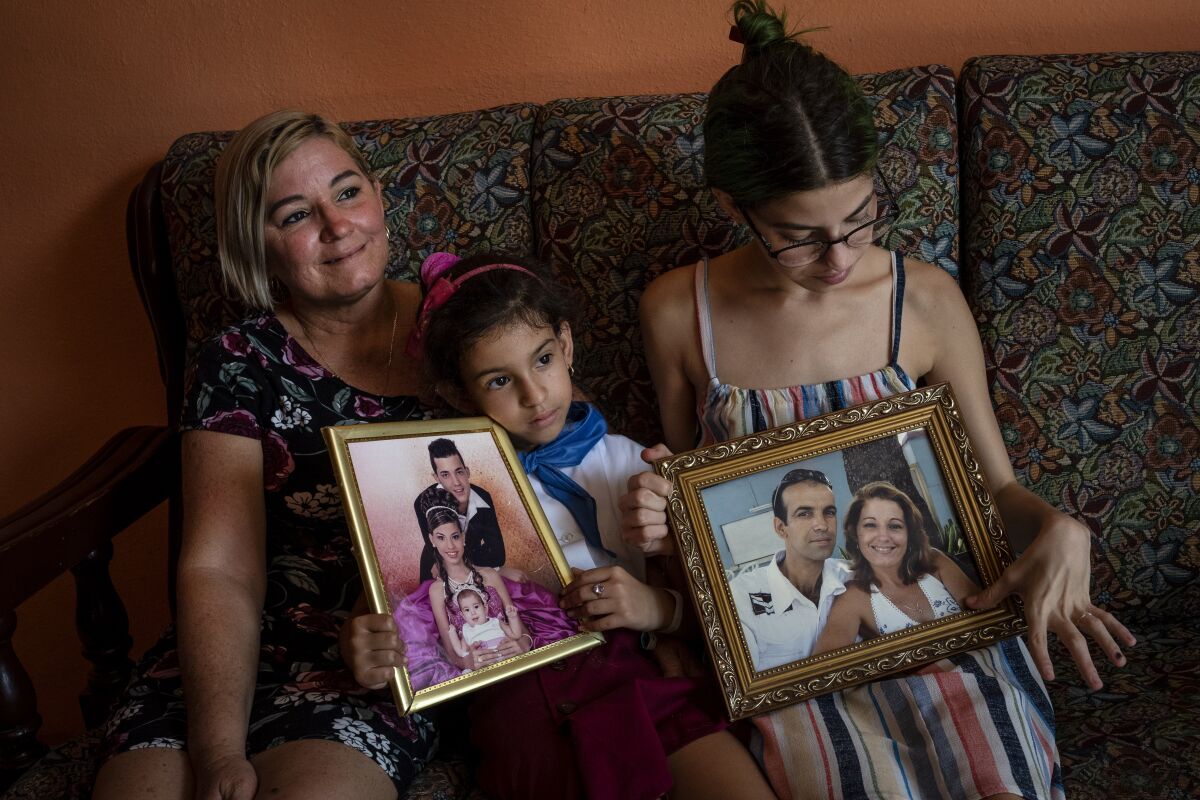 Danmara Triana, left, with her daughters Alice, center, and Claudia, show photos of them with their brother and father who moved to the United States in 2015, at their home in Cienfuegos, Cuba, Thursday, May 19, 2022. Separated families see hope in the measures announced by the U.S. administration of President Joe Biden, but the long wait of years and a web of political interests also makes them skeptical. (AP Photo/Ramon Espinosa)