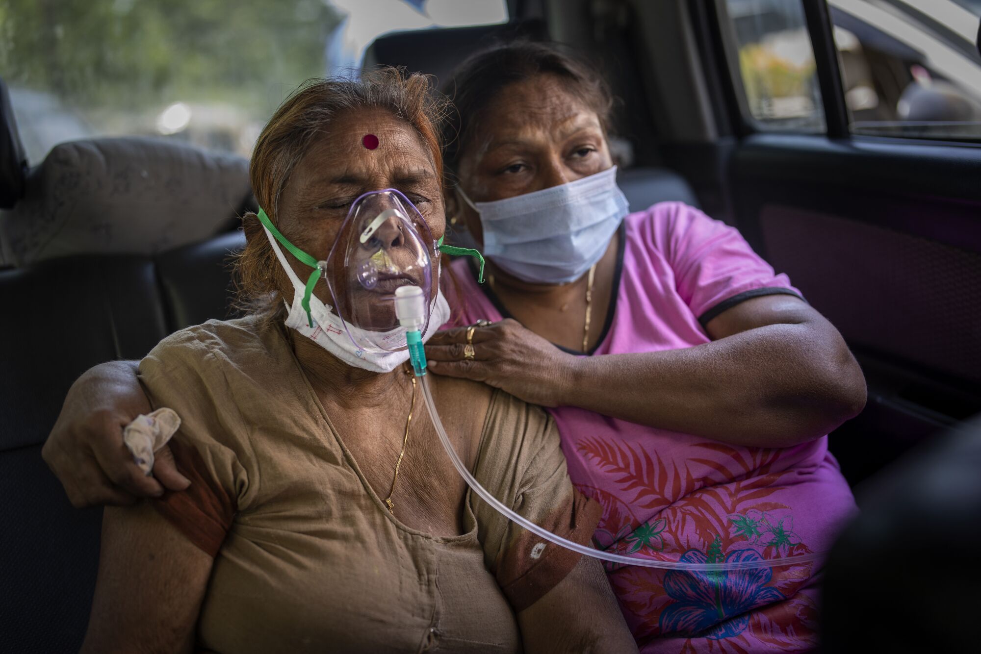 A COVID-19 patient, left, receives oxygen inside a car. With her is another woman.