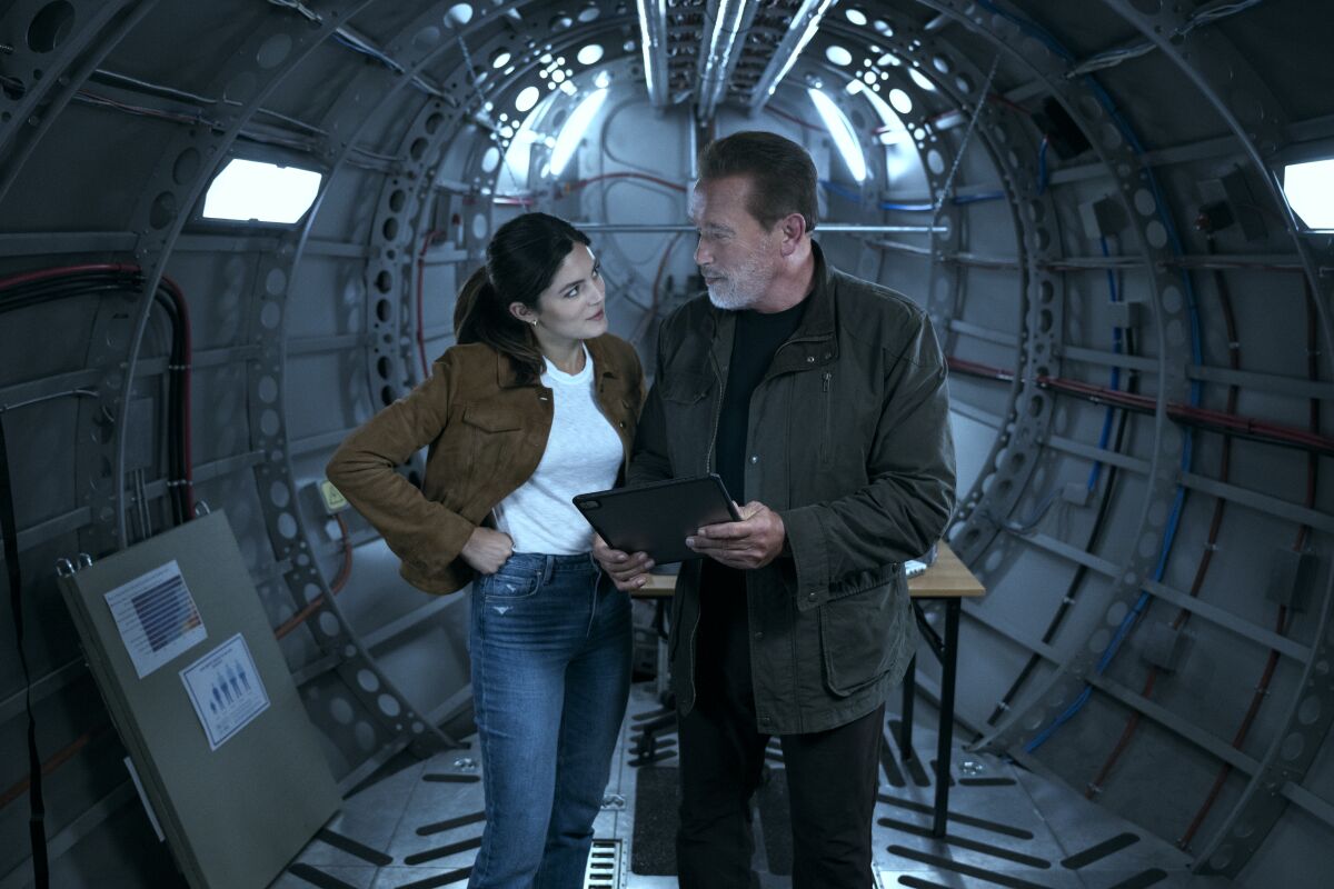 Monica Barbaro as Emma Brunner and Arnold Schwarzenegger as Luke stand and look at one another.