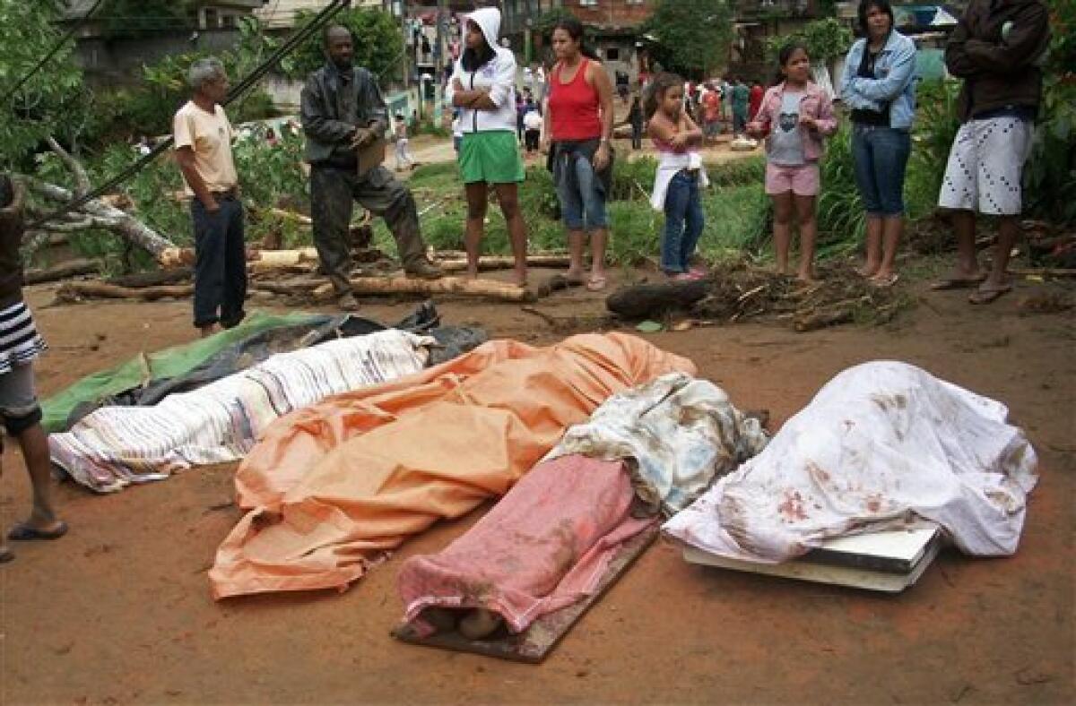 People stand by the bodies of mudslide victims after heavy rain in the neighborhood of Caleme in Teresopolis, Brazil, Wednesday Jan. 12, 2011. Authorities in Rio de Janeiro say 58 people have died in the mudslides and flash floods that followed torrential rain overnight. The mayor of the mountain town of Teresopolis just north of Rio said in a statement Wednesday that 48 people died, and more than 1,000 have been left homeless. (AP Photo/Paulo Cezar, Agencia O Globo)