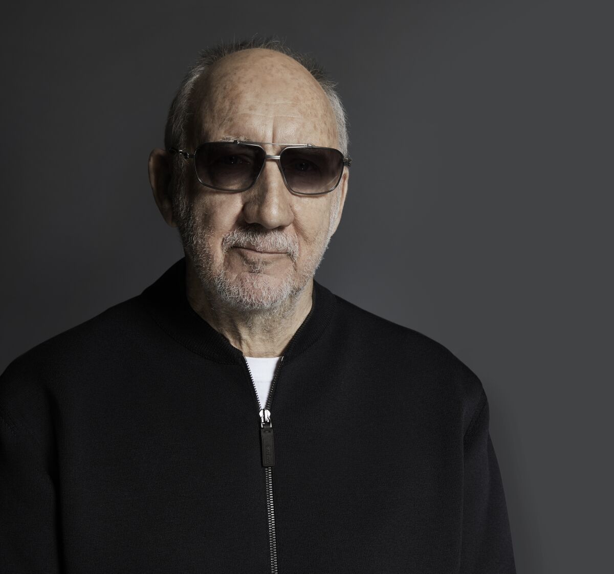A balding man in dark sunglasses and a dark zip-up shirt.