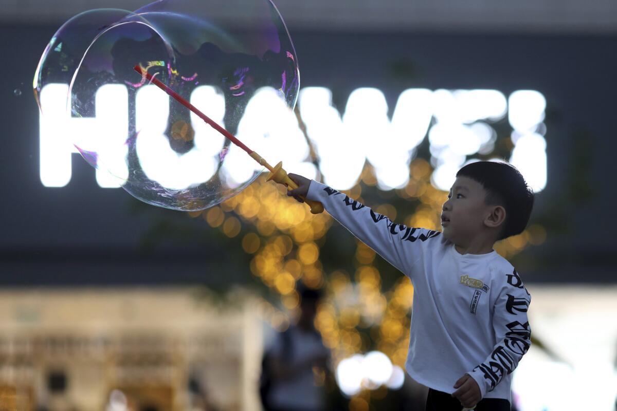 En esta imagen, tomada el 20 de mayo de 2019, un niño juega con pompas de jabón cerca del logo del gigante tecnológico chino Huawei, en Beijing. (AP Foto/Ng Han Guan)