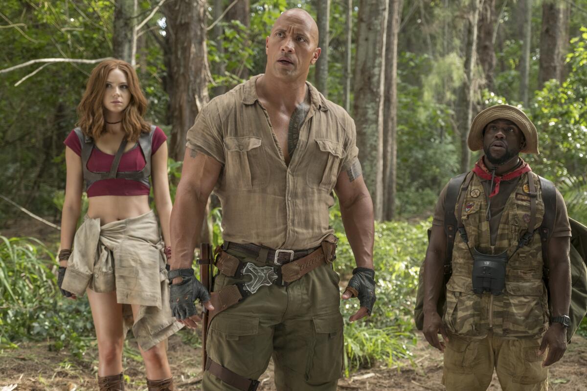 Karen Gillan, Dwayne Johnson and Kevin Hart in explorer gear standing in a jungle