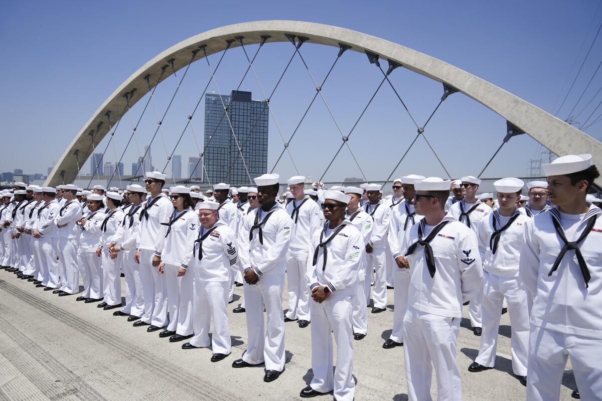 People in white uniforms form several lines on a road.