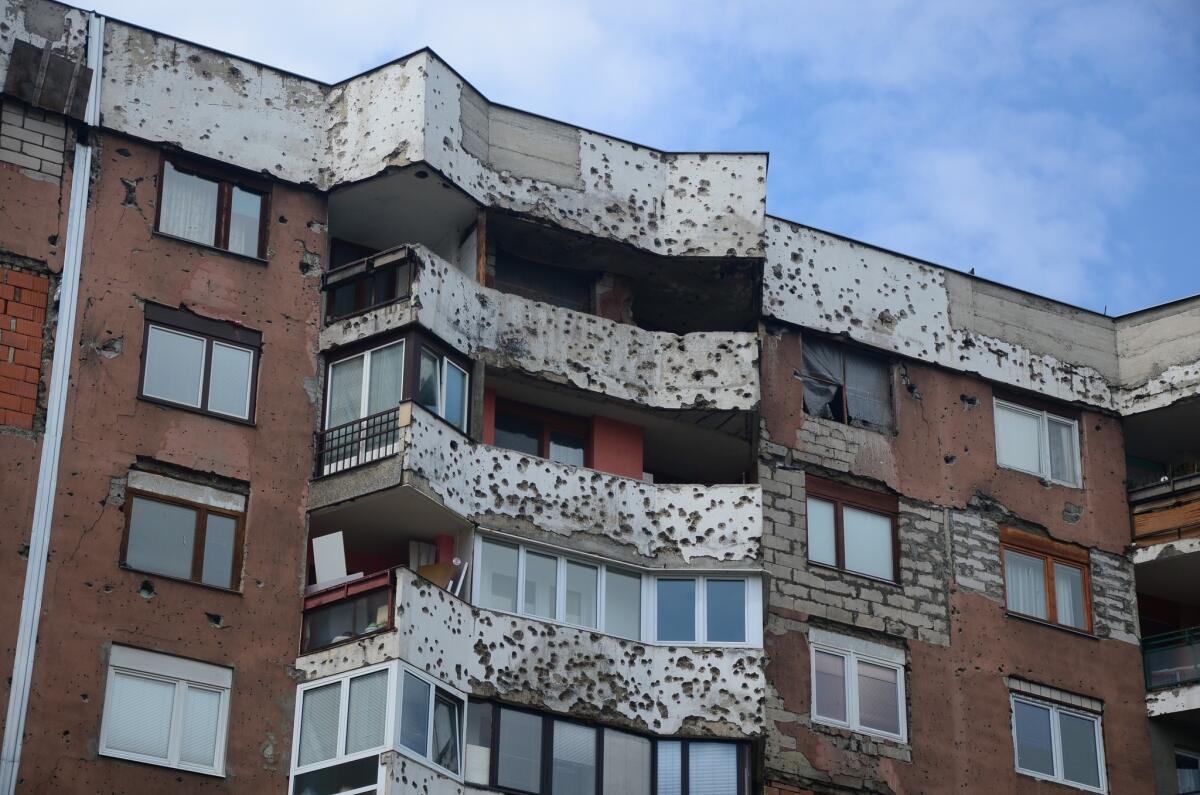 On many Sarajevo apartment buildings that were located near sniper positions in the siege of the early 1990s, scars from shelling remain, and sometimes makeshift window coverings as well.