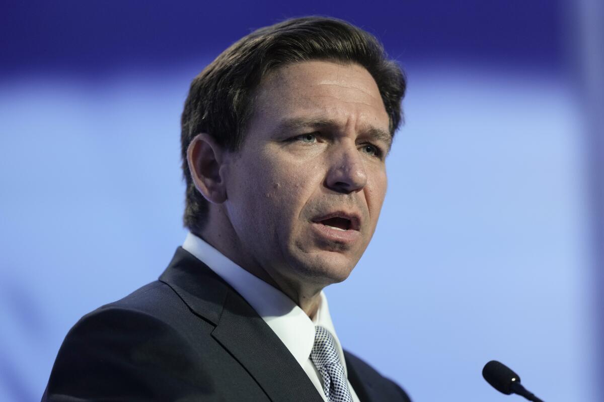Ron DeSantis wears a suit while speaking into a microphone. 