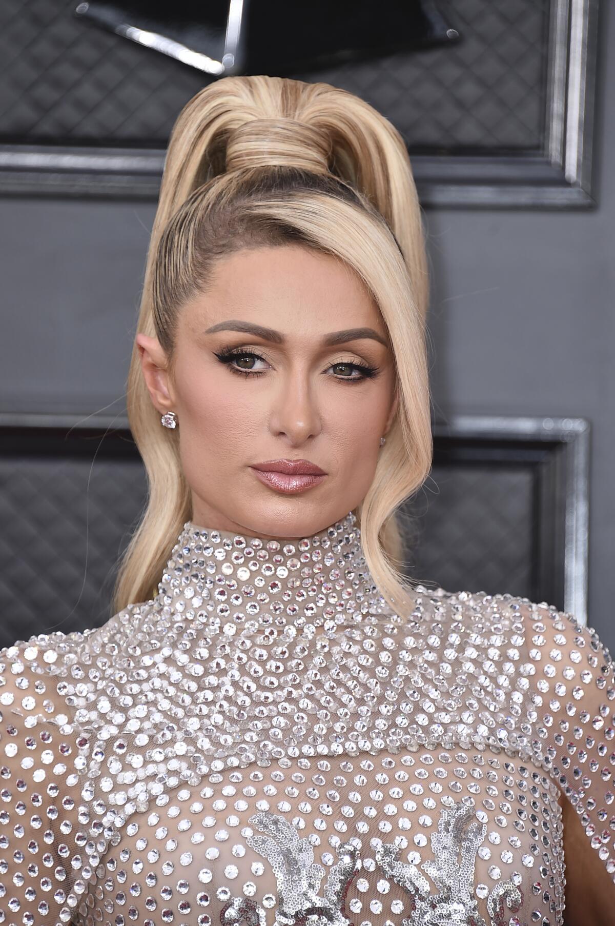 A woman with a long blond ponytail poses in a silver dress