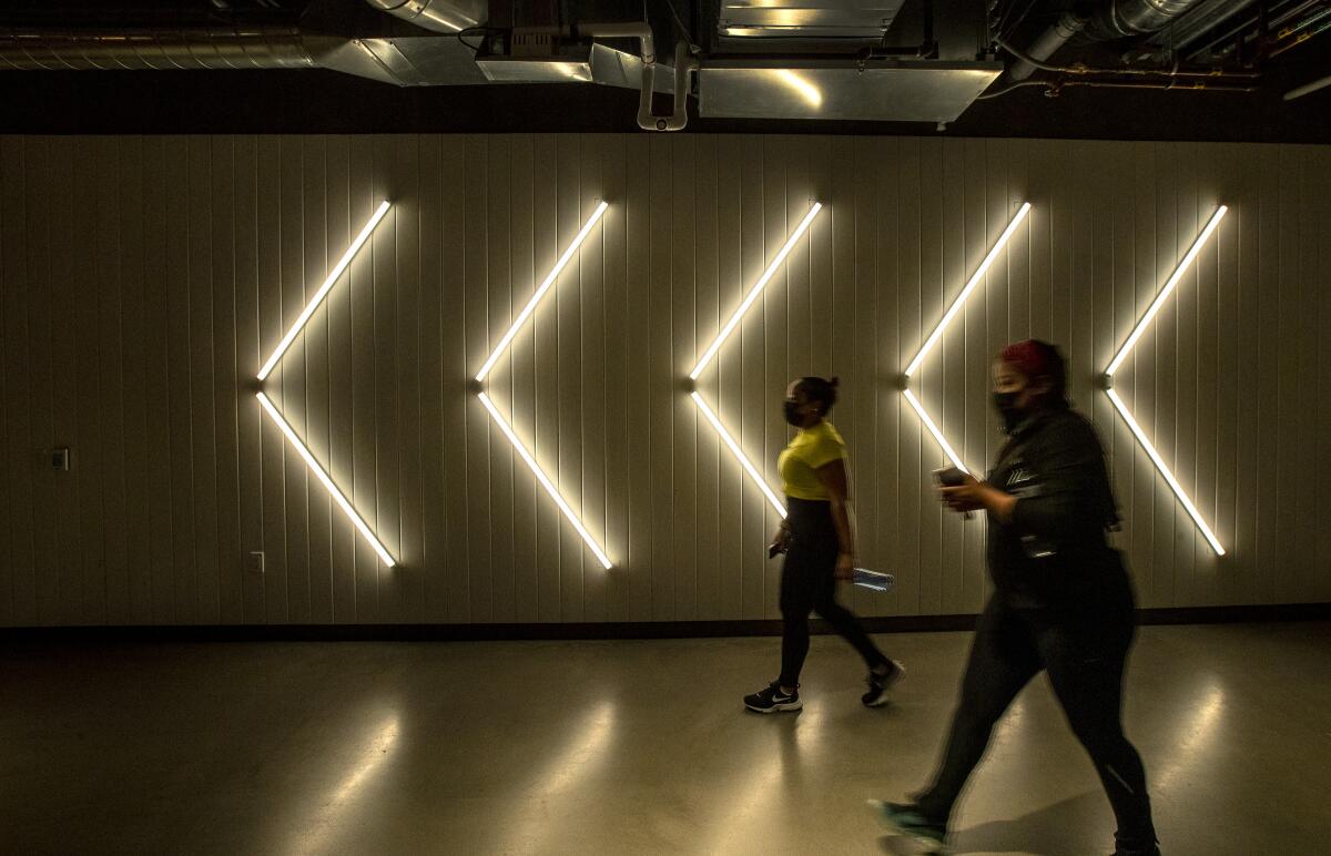 People walk past white neon light arrows on a wall