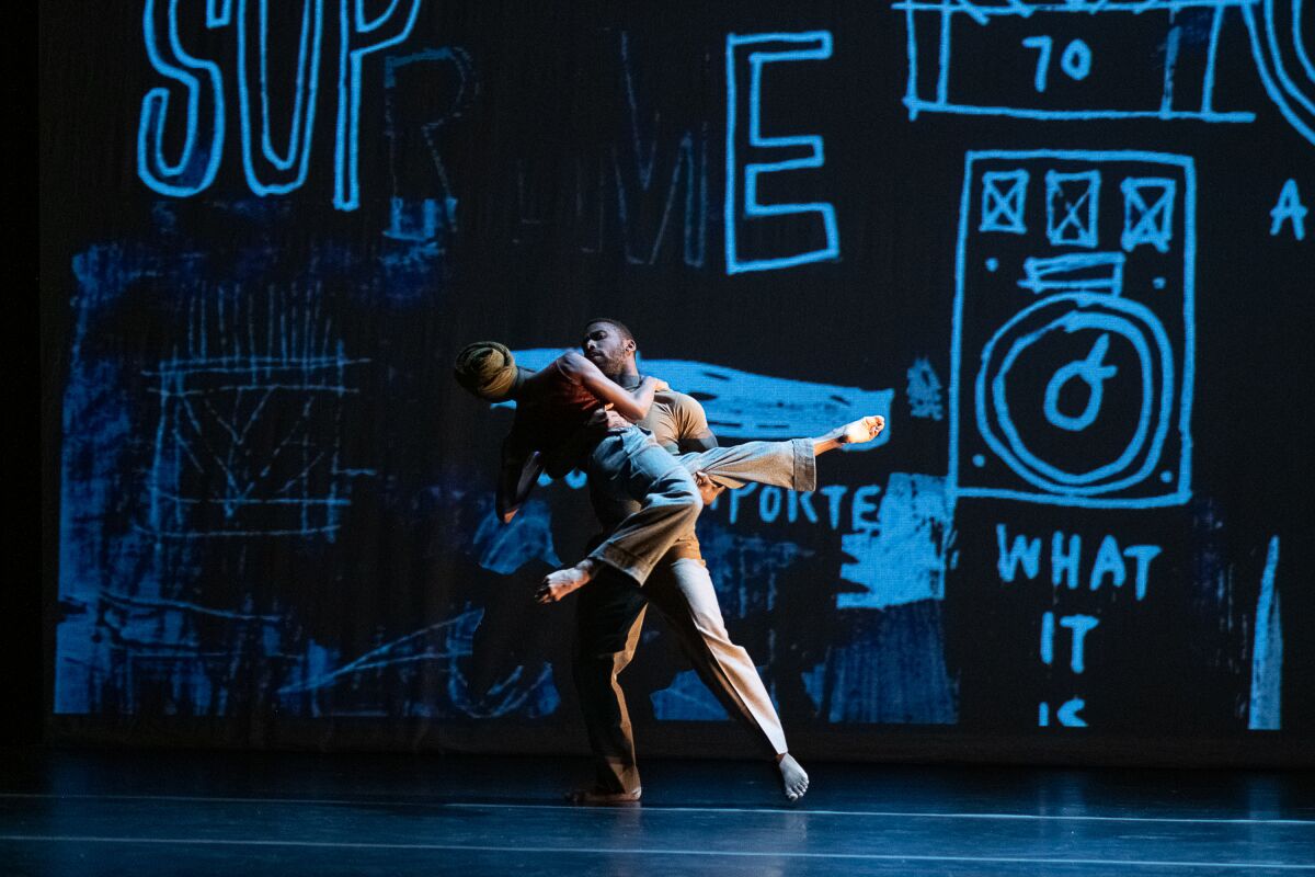 Two dancers move in front of a towering scrawl of images.