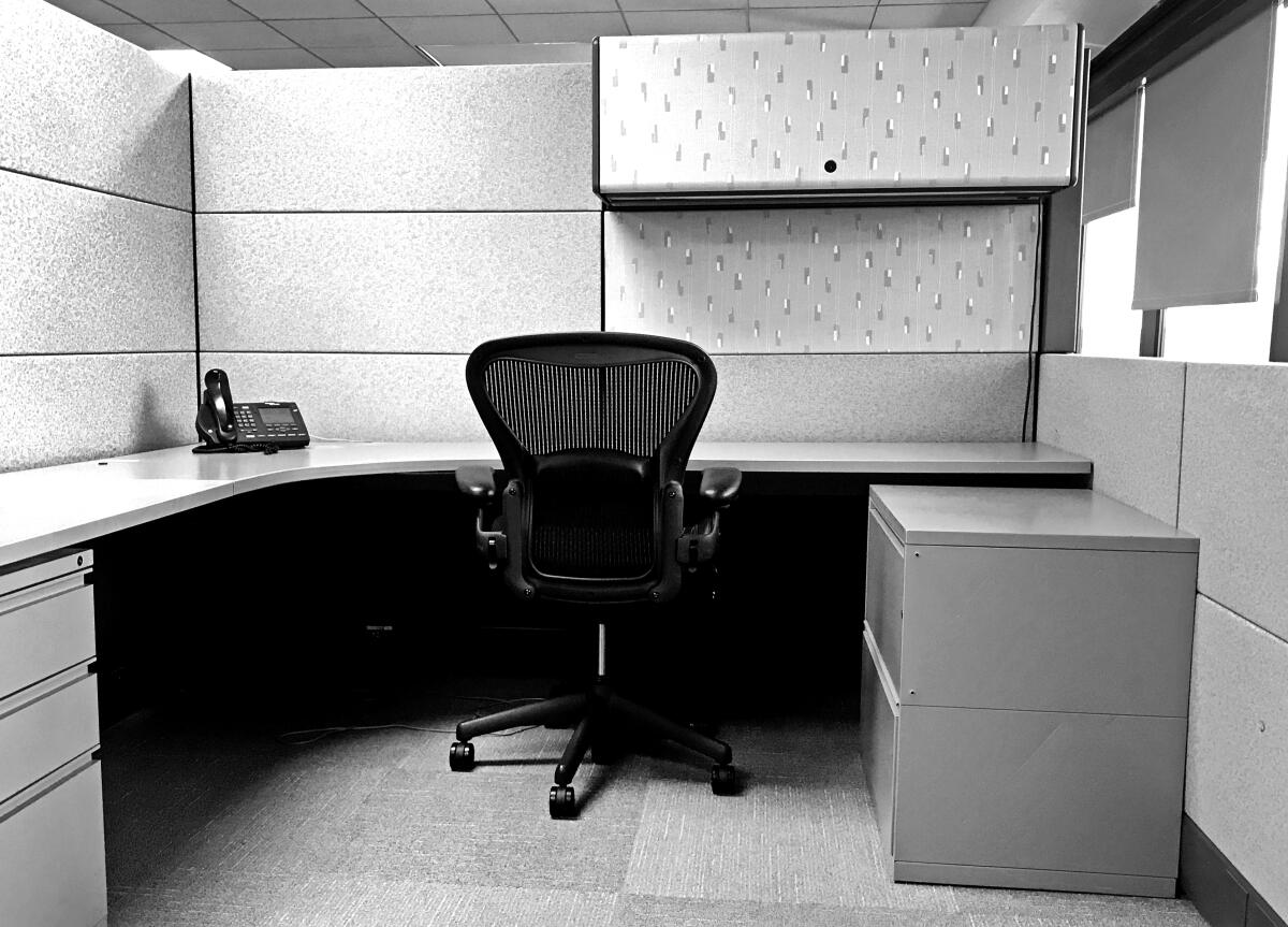 An empty office cubicle with a chair and a desk. 
