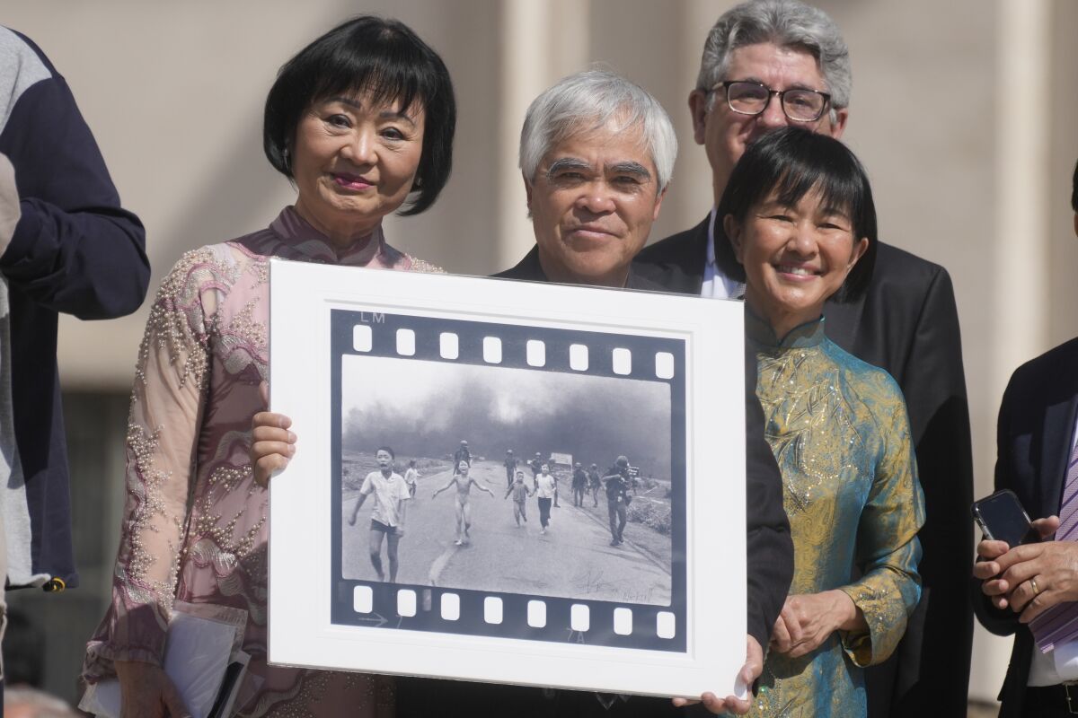 Pulitzer Prize-winning photographer Nick Ut, center, flanked by Kim Phuc, left, holds the" Napalm Girl", his Pulitzer Prize winning photo as they wait to meet with Pope Francis during the weekly general audience in St. Peter's Square at The Vatican, Wednesday, May 11, 2022. Ut and UNESCO Ambassador Kim Phuc are in Italy to promote the photo exhibition "From Hell to Hollywood" resuming Ut's 51 years of work at the Associated Press, including the 1973 Pulitzer-winning photo of Kim Phuc fleeing her village after it was accidentally hit by napalm bombs dropped by South Vietnamese forces. (AP Photo/Gregorio Borgia)