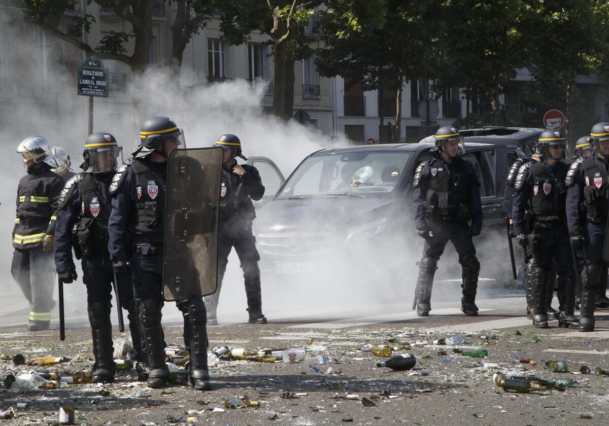 Police officers stand next to a burned car during a taxi drivers demonstration in Paris. French taxis are on strike around the country, after weeks of rising tensions over Uber's ride-share service.