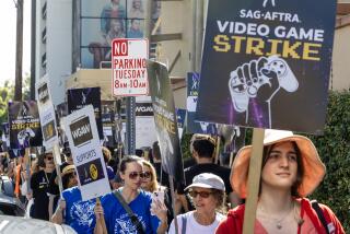 A bunch of people carrying picket signs and walking in a line past a building and "NO PARKING" sign