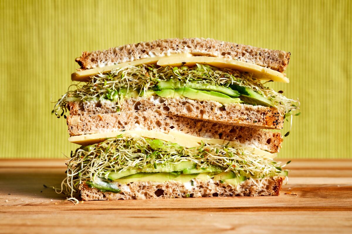 Two stacked halves of a sandwich on wheat bread filled with cheese, sprouts and avocado