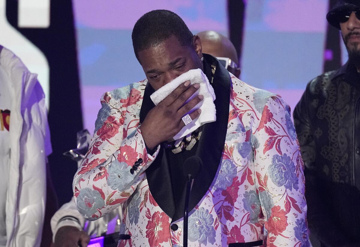 Busta Rhymes crying into towel while on stage, wearing a flowered blazer 