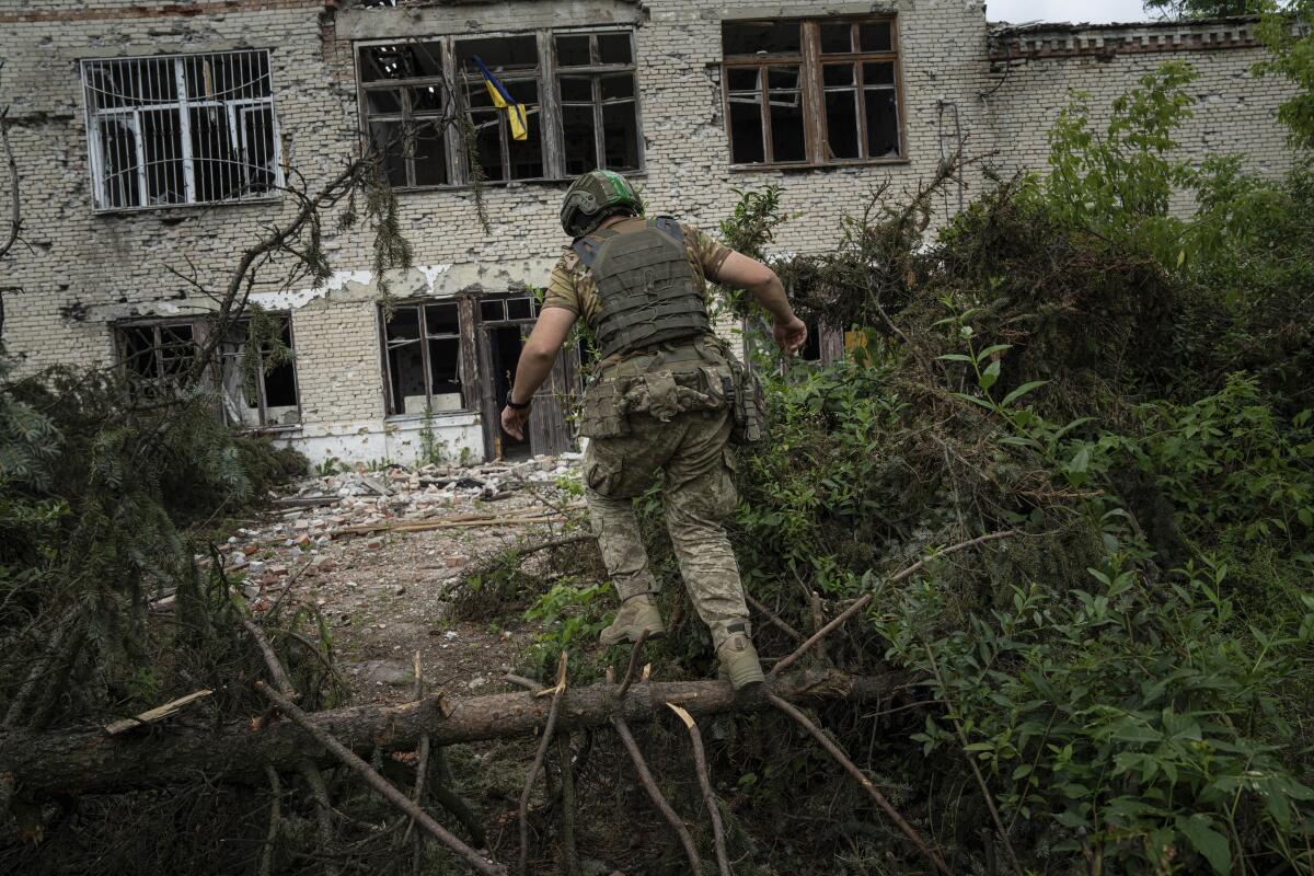 a soldier climbs over a fallen tree amid rubble 