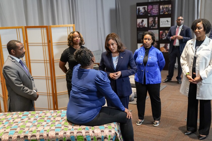   Vice President Kamala Harris talks to a seated woman as other look on.