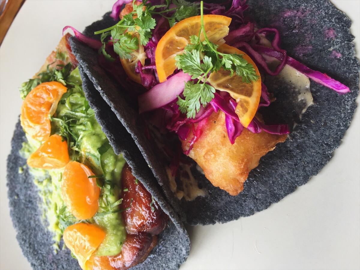 One carnitas and one fish taco, served on handmade blue corn tortillas at Taco María.