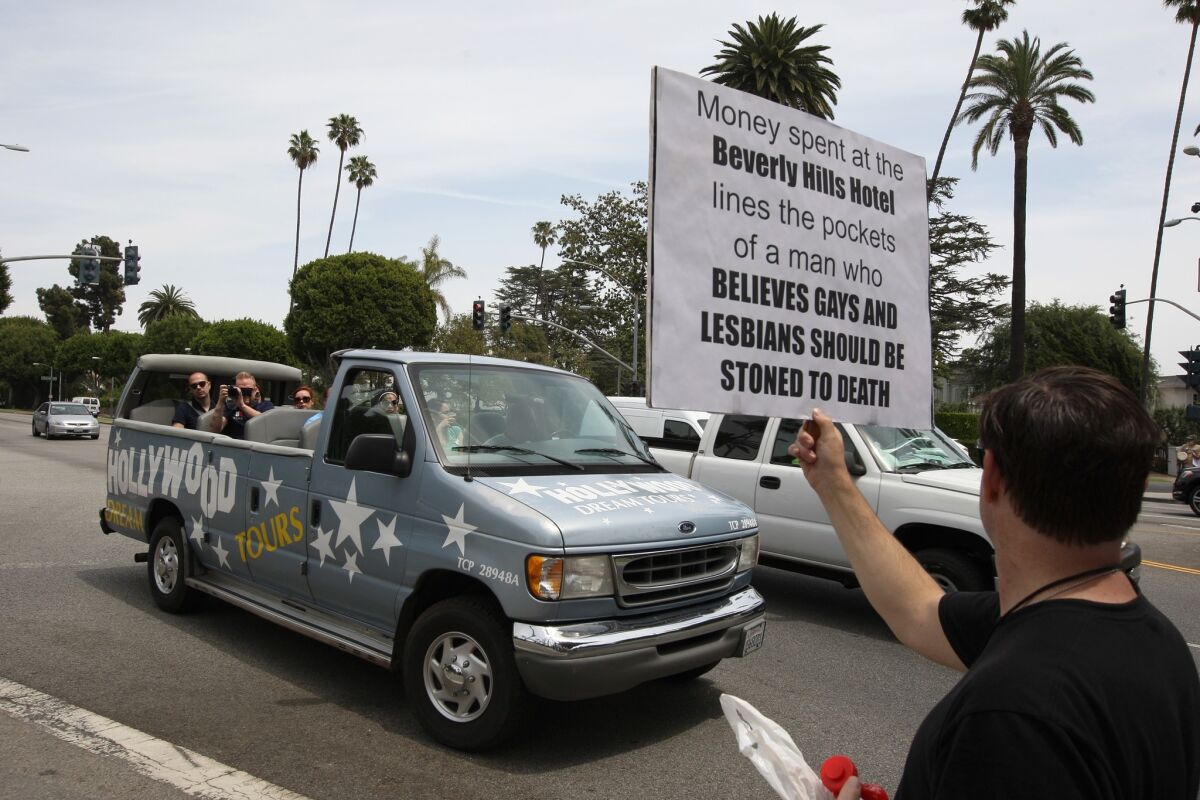 A tourist van slows down to look at a demonstrator protesting draconian punishment of gay people announced by the Sultan of Brunei at the entrance to the Beverly Hills Hotel, which the Sultan owns.