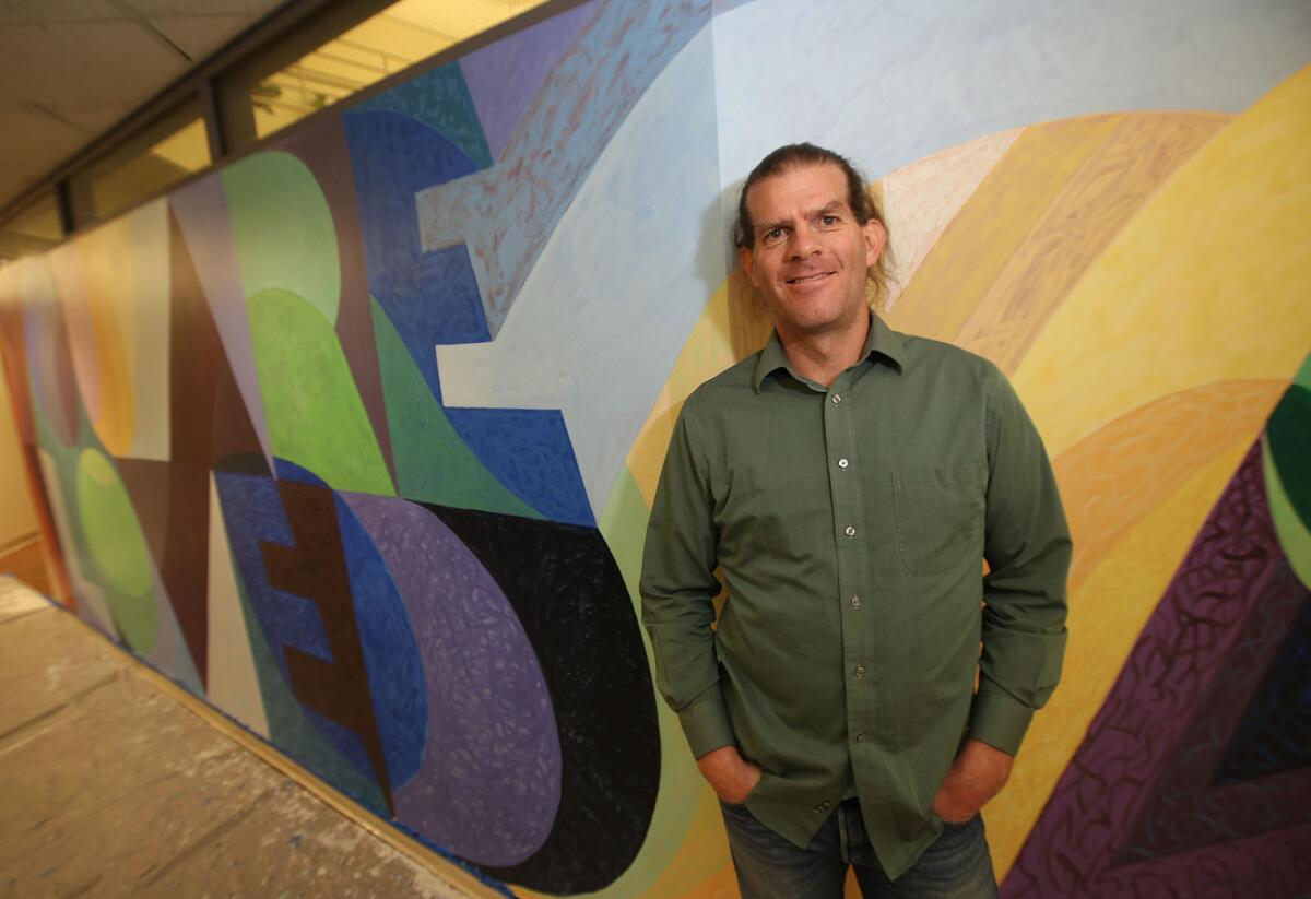 Artist Alex Cook stands in front of his newest "You Are Loved" mural in the Social Ecology I building at UC Irvine. The project is part of the UCI School of Social Ecology's efforts to promote compassion.