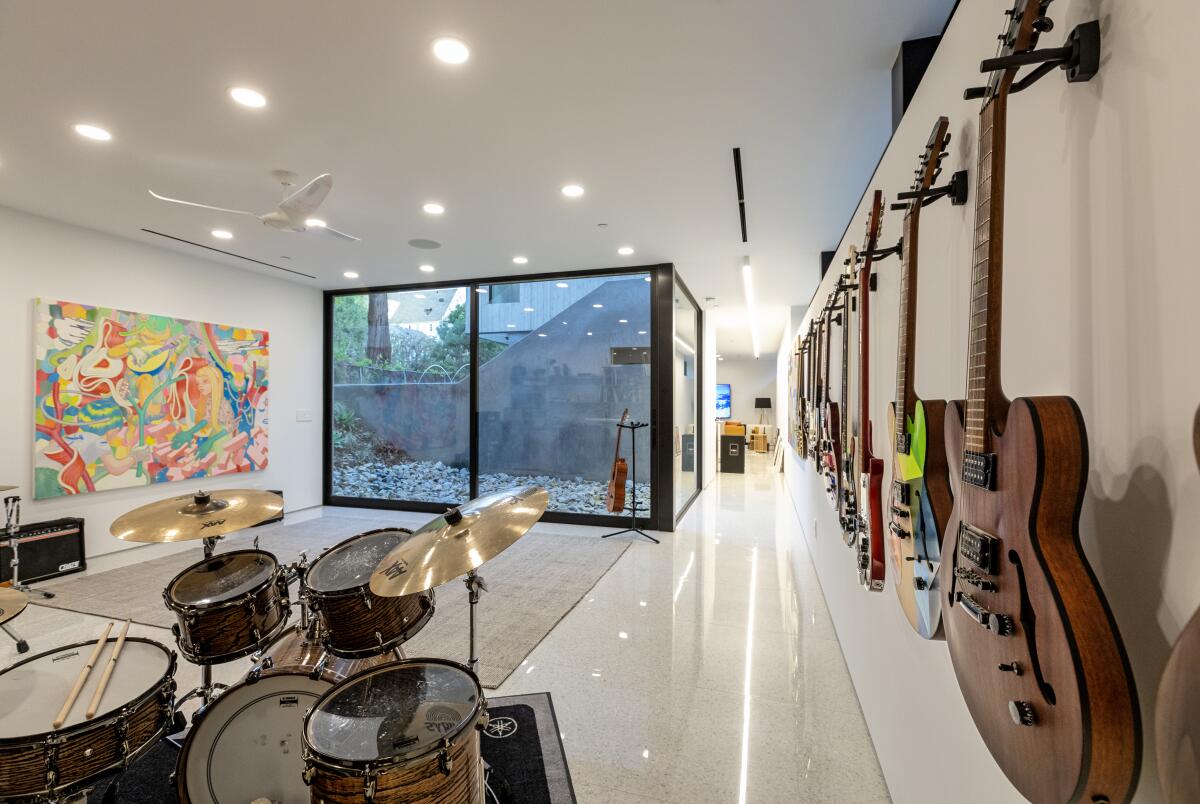 A room with a drum set, painting and guitars on the wall and a view of the greenery outside.