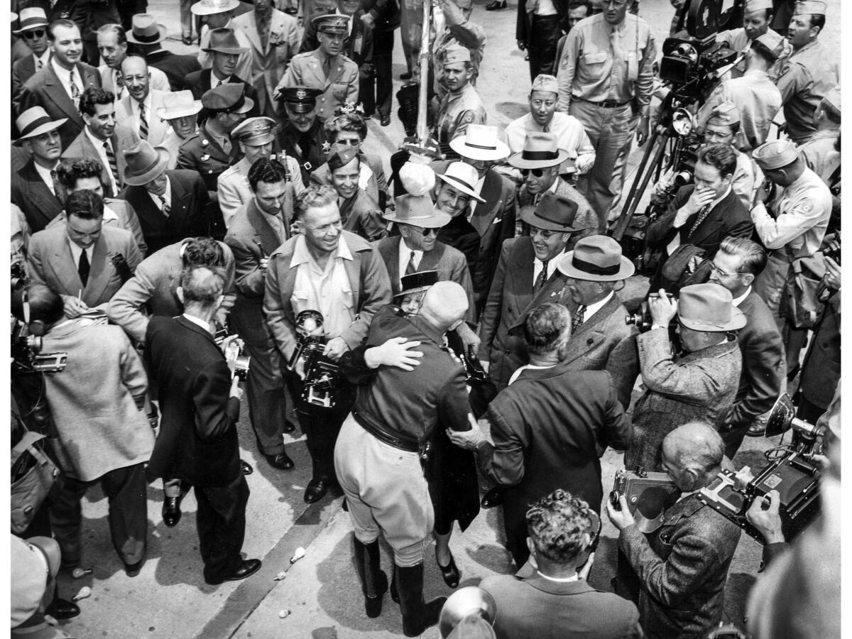 June 9, 1945: Photographers swarm Gen. George S. Patton Jr. as he embraces Mrs. Frances P. Graves, mother of Lt. Francis P. Graves Jr., Patton's aide, at the airport on his arrival. Lt. Graves stands to Patton's right.