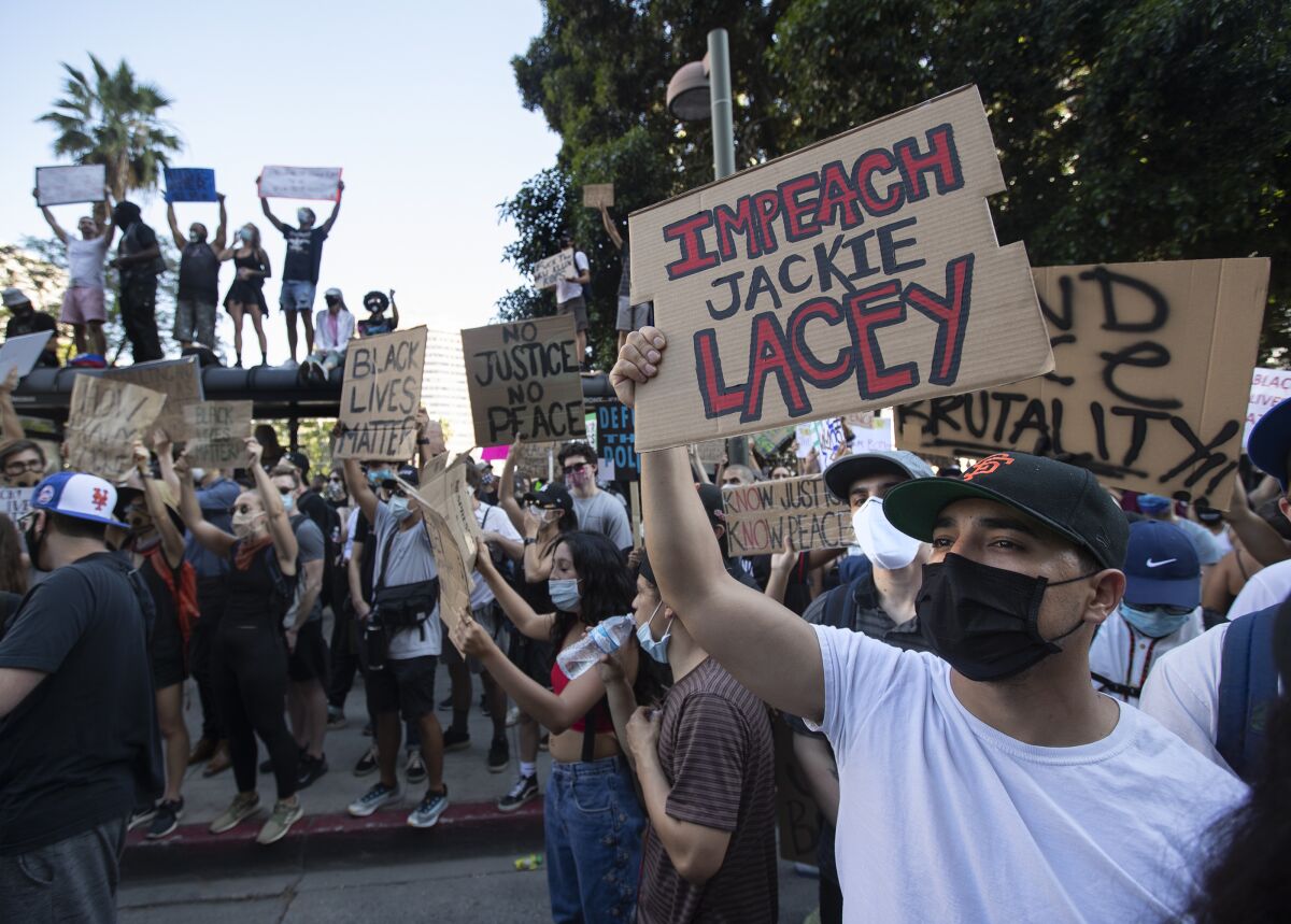 Paul Villalobos holds a sign that reads "Impeach Jackie Lacey" on Spring Street in downtown Los Angeles