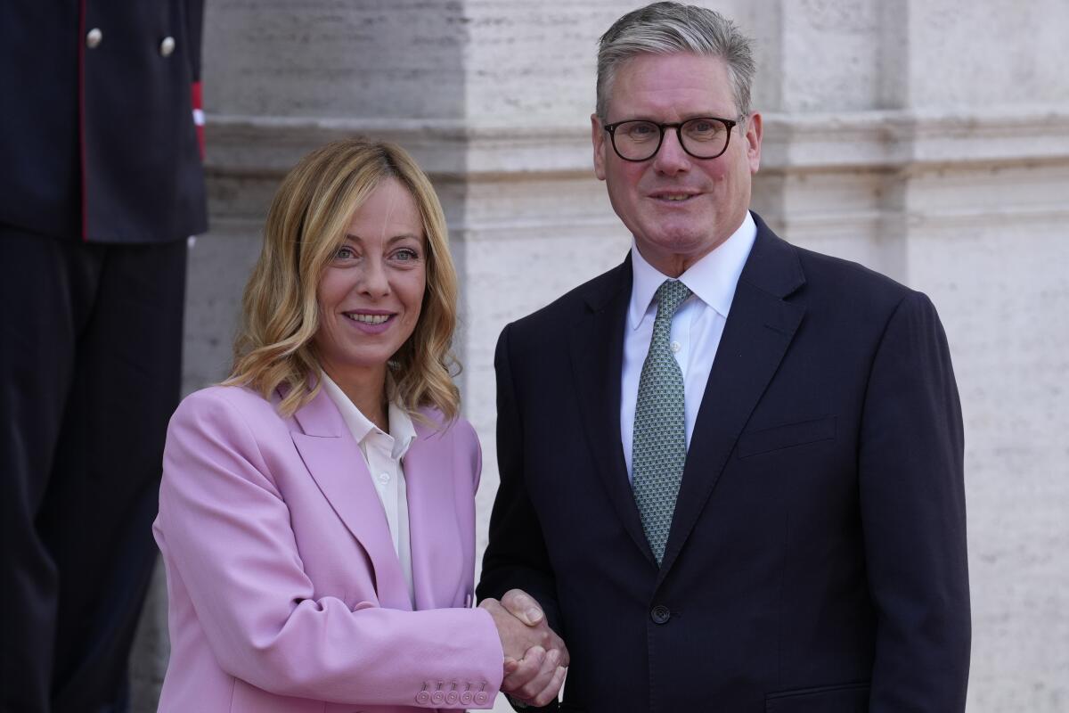 Italian Premier Giorgia Meloni, left, in a purple suit, shakes hands with Keir Starmer in a black suit.