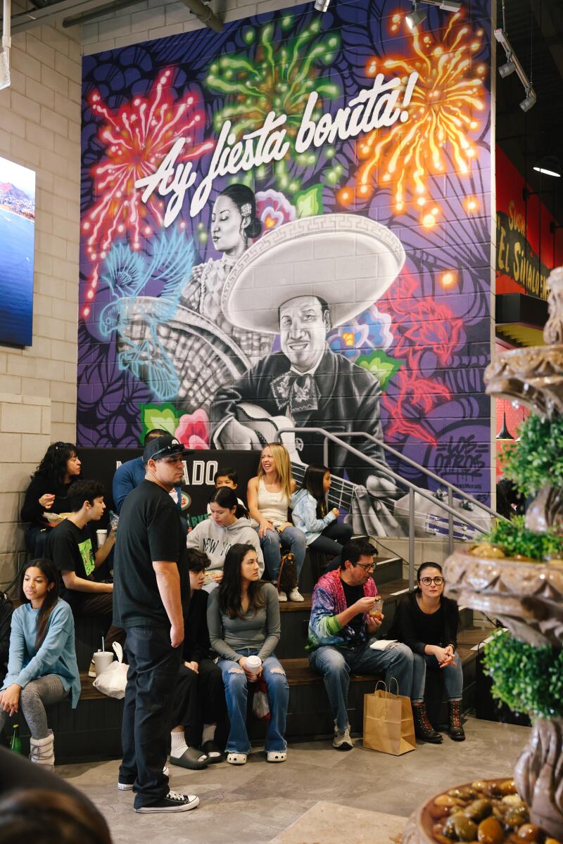 A group of people sitting in front of a colorful indoor mural that reads "ay fiesta bonita!" 