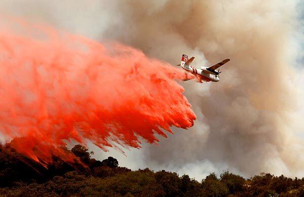 A plane drops Phos-Chek fire retardant to help slow the flames.