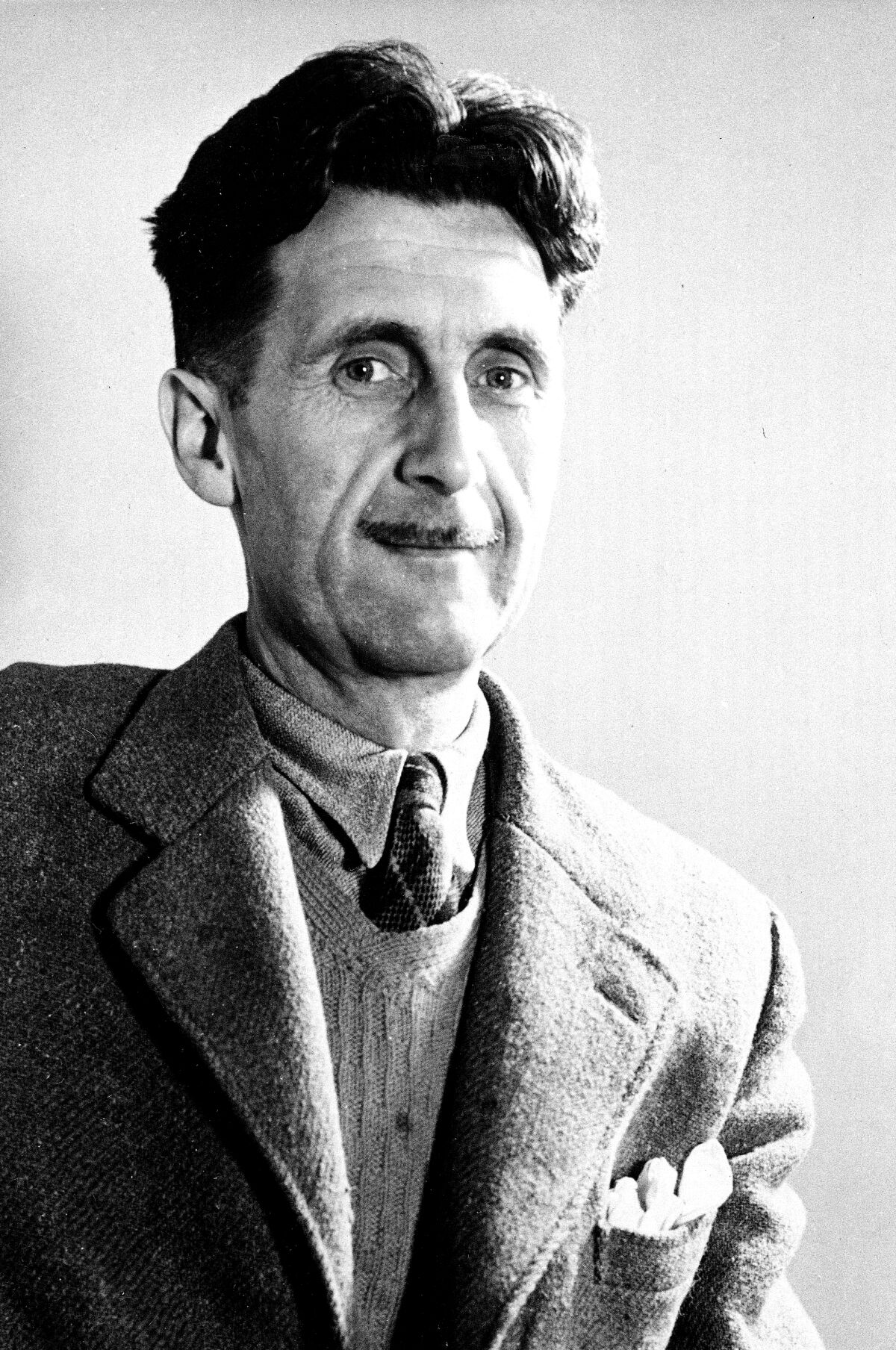 A black and white photo of a man grinning in a suit and sweater.