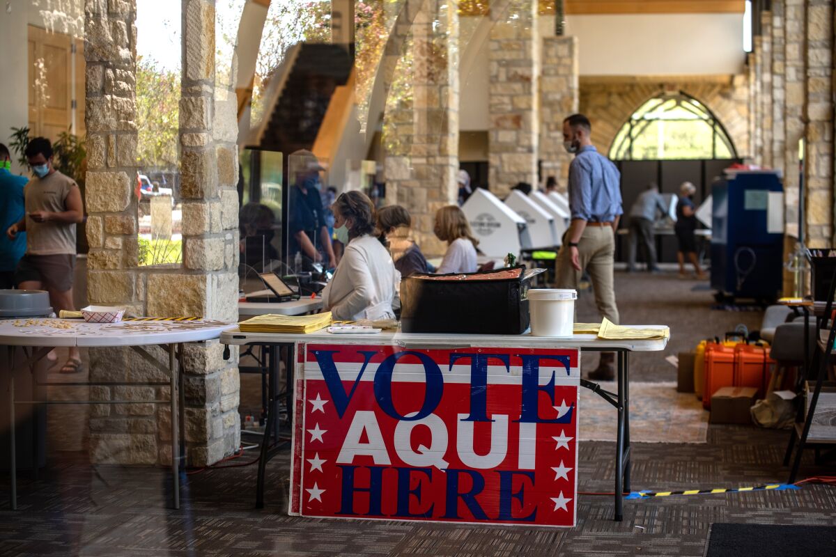 Volunteers help early voters cast ballots at a busy courtyard polling site in Austin, Texas. A sign reads "Vote aquí/here."