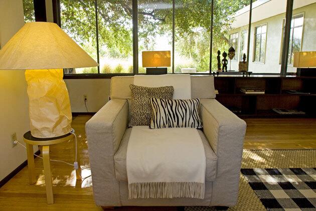 For this living room chair, the designer folded a white throw into a long strip, laid down the middle of the seat. The graphic treatment echoes the graphic lines of the checked rug. The paper lamp is by Ingo Maurer. Herrington says the shade fits with the clean lines and contemporary look of the home.