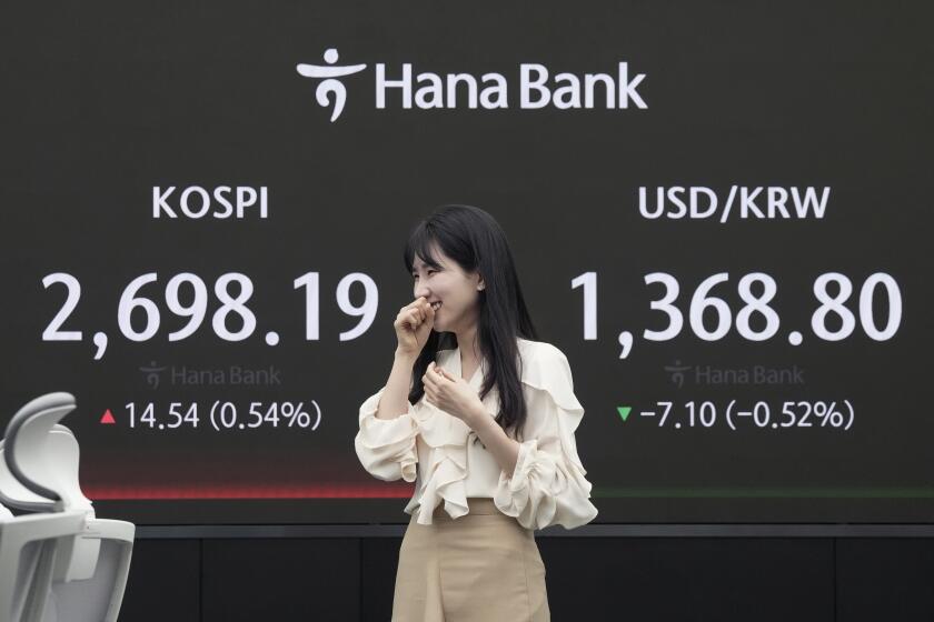A currency trader smiles near the screen showing the Korea Composite Stock Price Index (KOSPI), left, and the foreign exchange rate between U.S. dollar and South Korean won at the foreign exchange dealing room of the KEB Hana Bank headquarters in Seoul, South Korea, Friday, May 3, 2024. (AP Photo/Ahn Young-joon)
