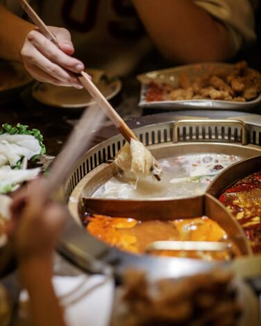 A hand uses chopsticks to stir meat in a pot of broth 